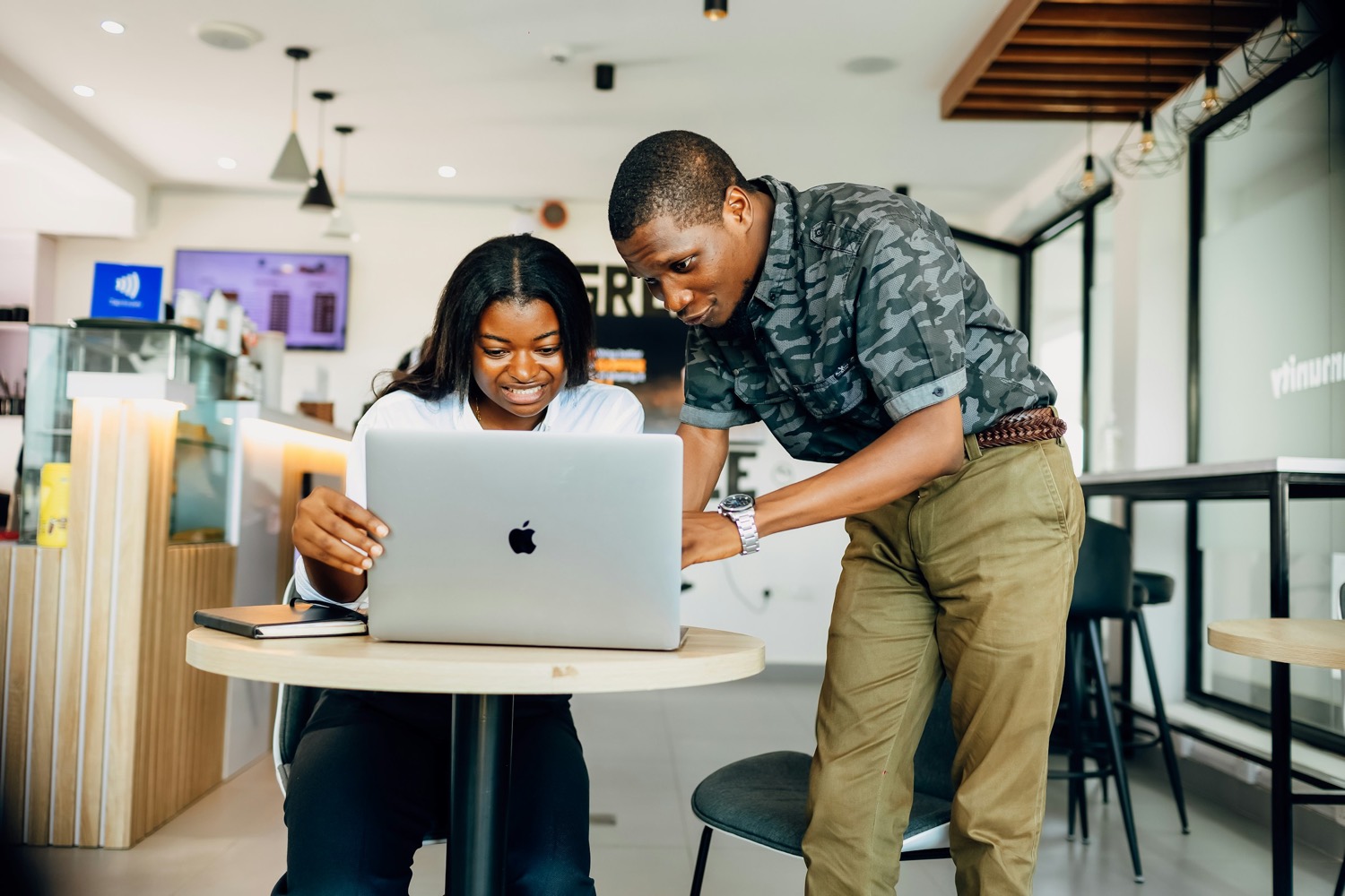 A colleague helping a teammate at her laptop in a bright office